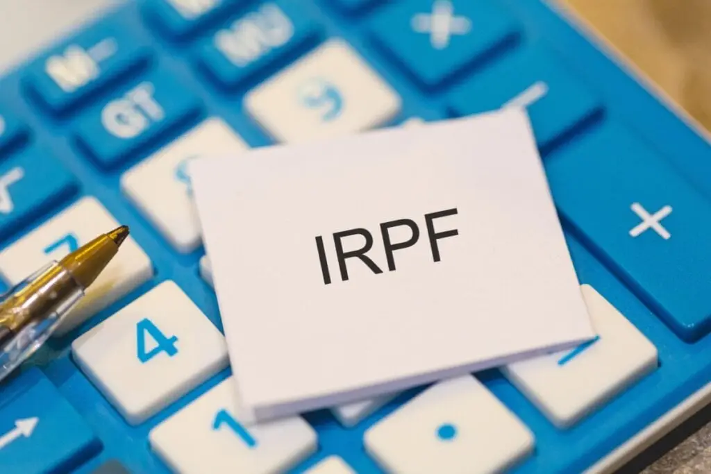 Papel com as letras "IRPF" em cima de uma calculadora azul e branca