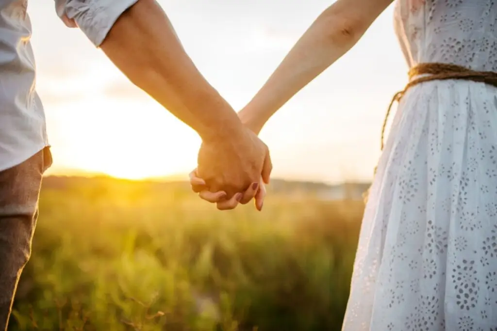 Foto com foco nas mãos dadas de um casal ao pôr do sol 