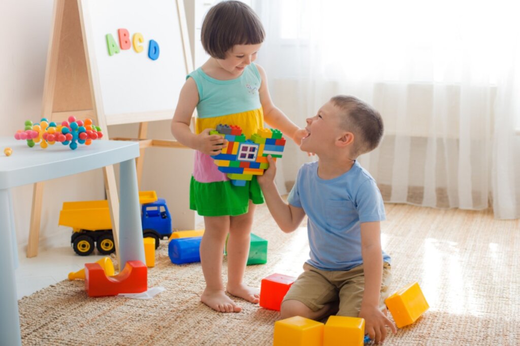 Crianças pequenas interagindo enquanto compartilham um brinquedo de blocos coloridos em um ambiente lúdico