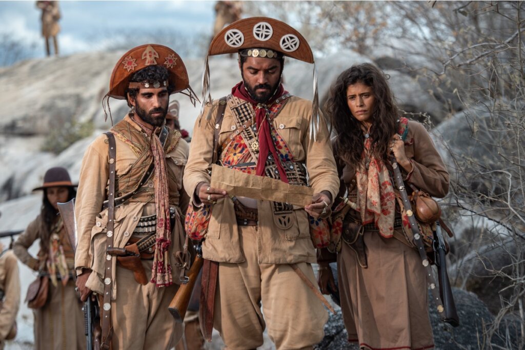 Cena dramática de "Guerreiros do Sol" com personagens observando um mapa no sertão