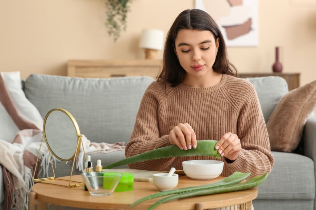 Jovem mulher fazendo cosméticos orgânicos com aloe vera perto da mesa na sala de estar
