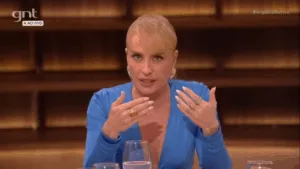 Angélica de cabelo preso, franja e vestido azul claro de mangas compridas