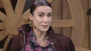 Michelle Barros de cabelo preso, com jaqueta marrom e camisa xadrez