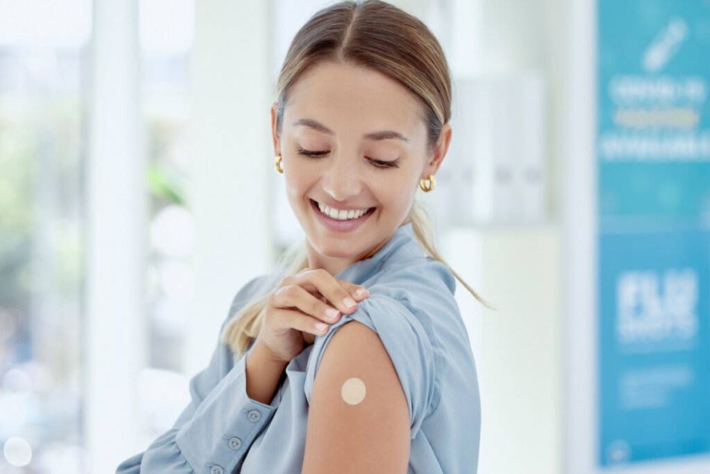 Mulher sorrindo, levantando manga de blusa azul e olhando para curativo de vacina no braço
