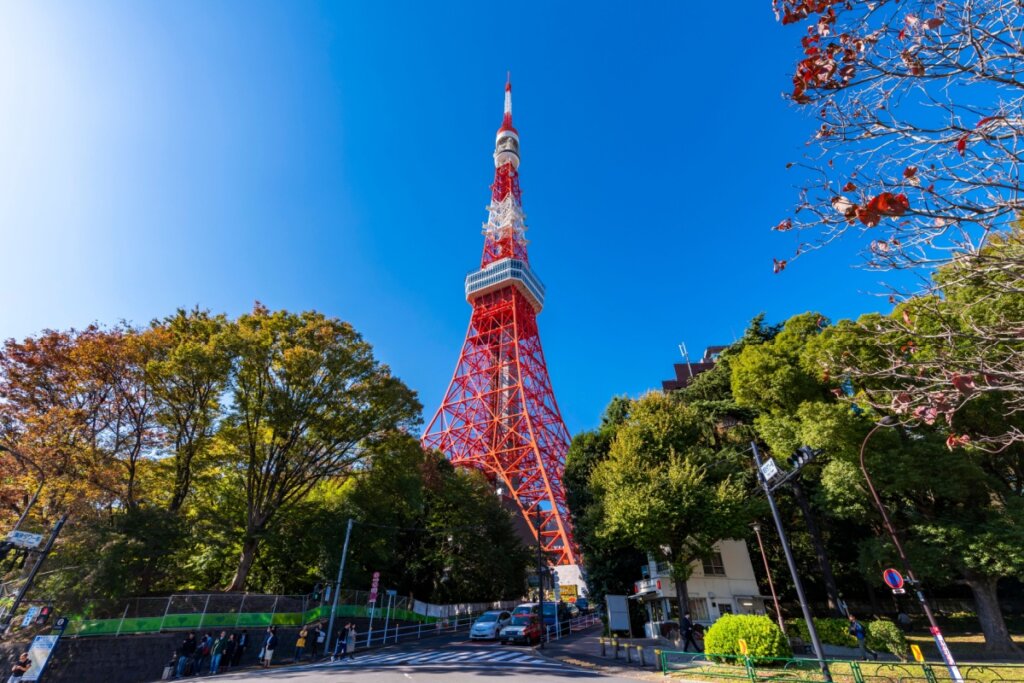 Imagem de uma torre alta em vermelho e branco no meio de parque na cidade de Tóquio
