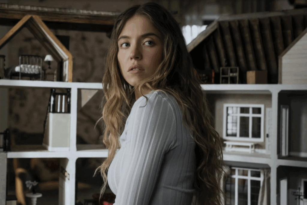 Mulher observando algo fora de quadro enquanto está posicionada diante de uma casa em miniatura com múltiplos compartimentos