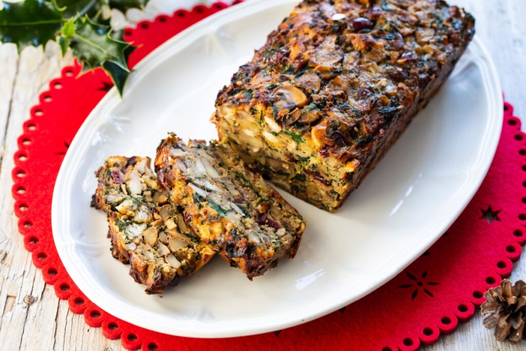 Assado de nozes servido em travessa de cerâmica branca em cima de jogo americano vermelho em cima de mesa de pedra branca
