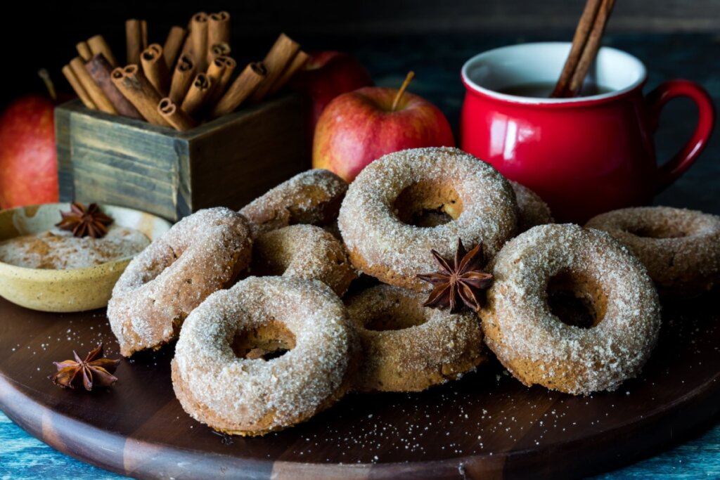 Donuts de maçã polvilhados com açúcar e canela em cima de uma tábua de madeira 