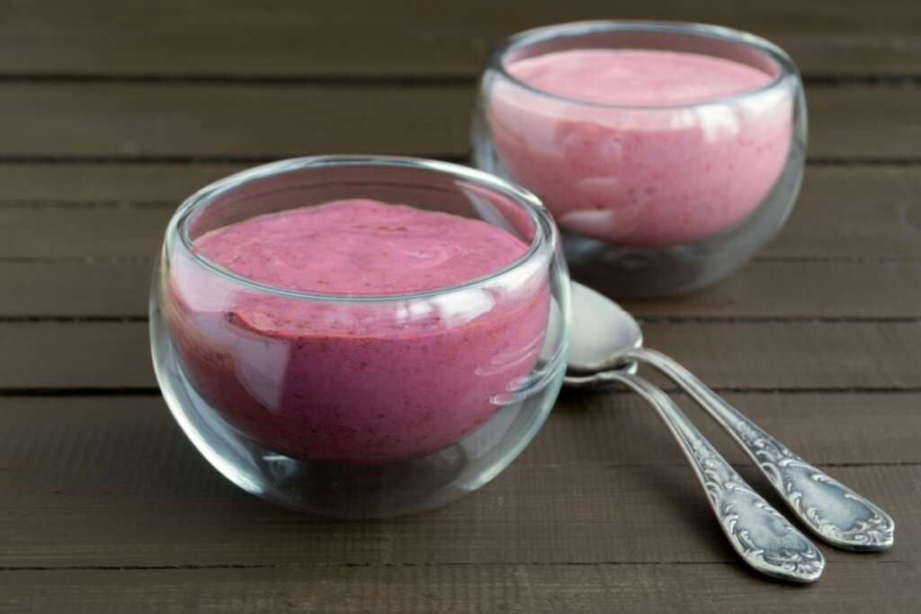 Dois recipientes de vidro com musse de uva e em cima de uma mesa de madeira