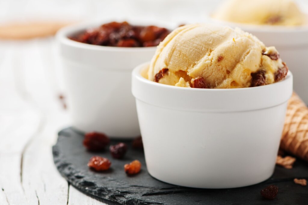 Recipiente branco com sorvete de passas ao rum e, ao lado, outro recipiente branco com uvas-passas 