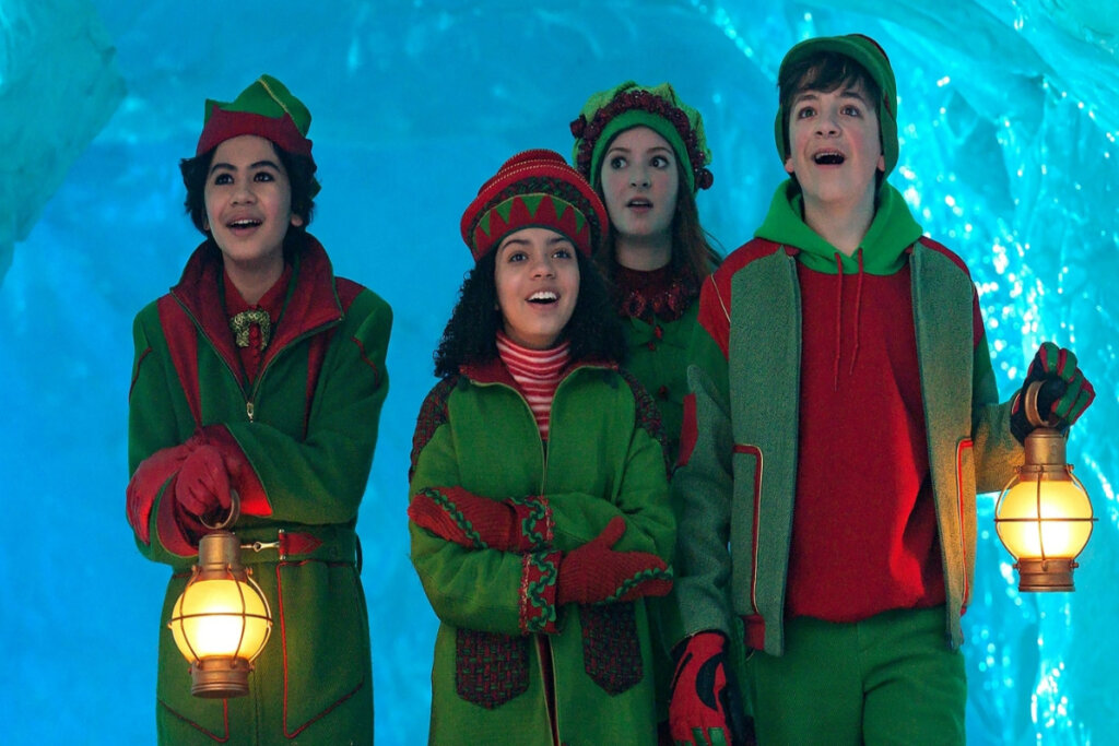 Quatro jovens, vestidos com roupas de duende verde e vermelho, com expressões deslumbradas