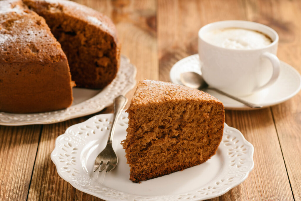 Pedaço de bolo de chocolate em cima de um prato branco em uma mesa de madeira com uma xícara de café