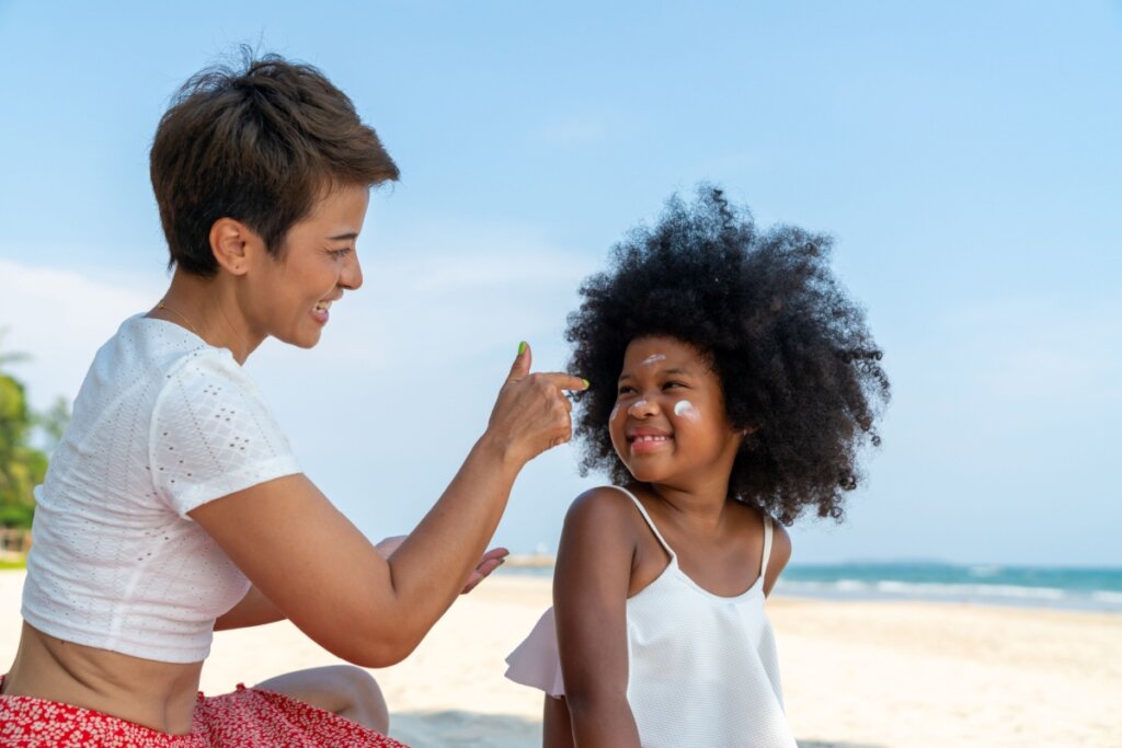 Adulta de cabelo curto passando protetor solar em criança na praia